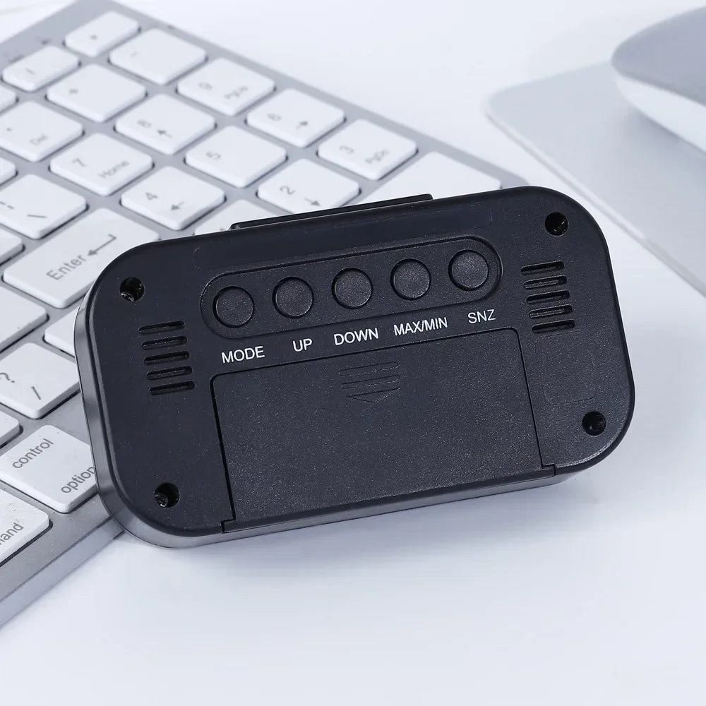 Schwarze Wetterstation-Uhr mit Farbdisplay; Rückseite mit MODE UP DOWN MAX/MIN SNZ-Tasten vor weißer Tastatur.